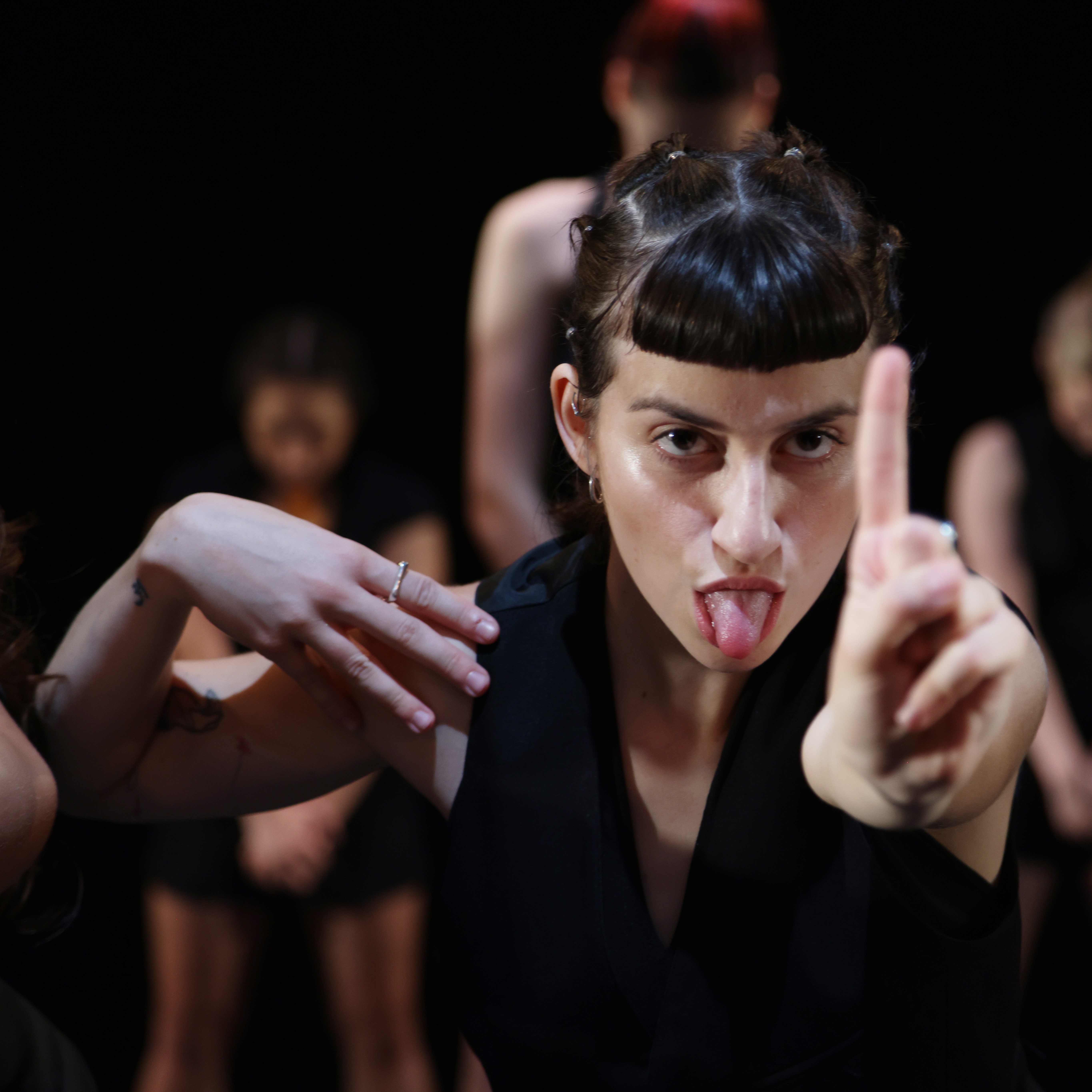dancer with black straight across fringe sticks her tongue out and holds a finger up