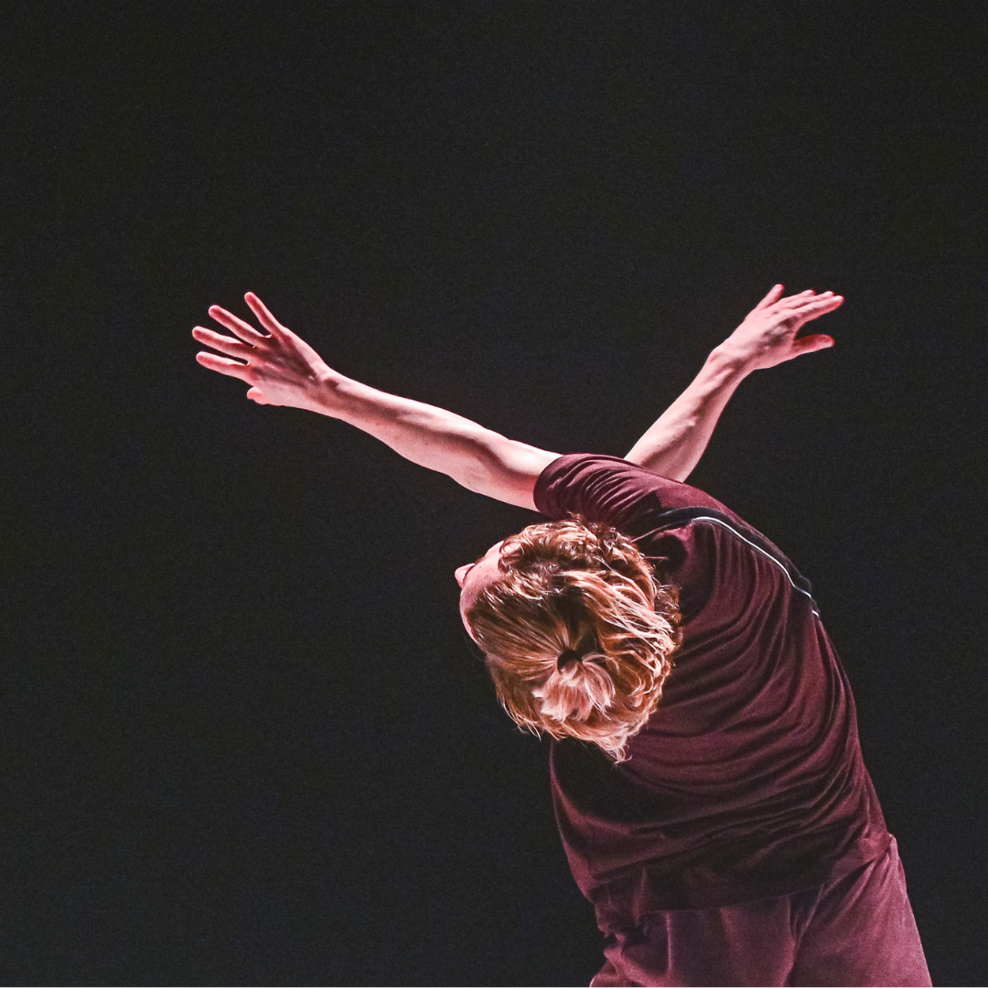 dancer in maroon twisting arms away and up