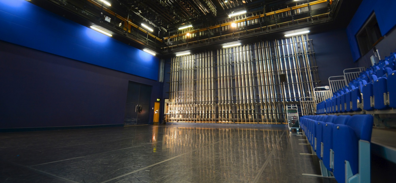 the blue room is a large dance studio with blue walls and blue fold down chairs that look soft. The floor is black dance lino and the lights are warm
