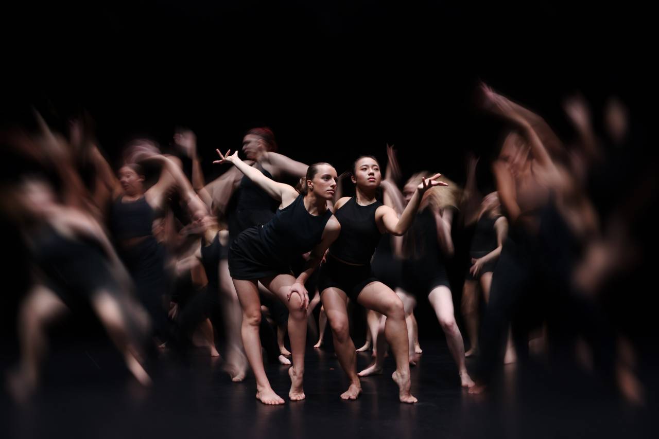dancers in black bending their knees, the dancers on the edge blurred with movement