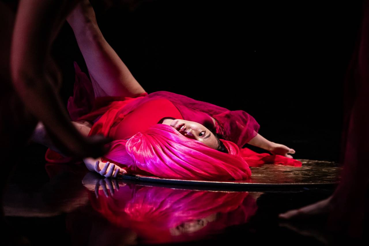 dancer in red shiny costume lies on the floor