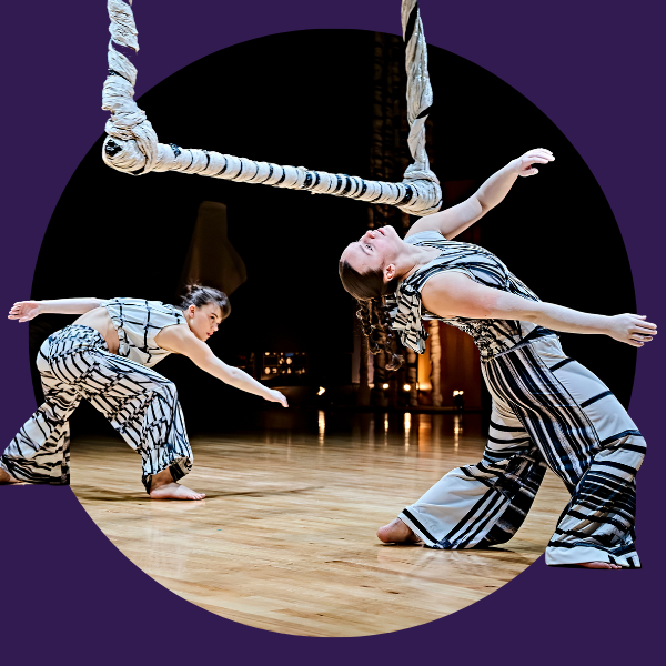 two dancers in white costumes printed with charcoal line drawings bend backwards under a swinging sculpture made of twisted paper that hangs from the roof