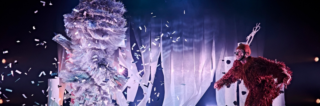 a dancer dressed as a deer joyfully dances around a stage with snowy winter set whilst another dancer covered head to toe in silver tassle trim covers the stage in silver confetti released from their costume as they move