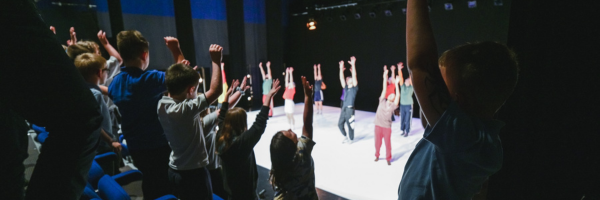 children watching a dance show, following the moves of the dancers, their hands in the air 