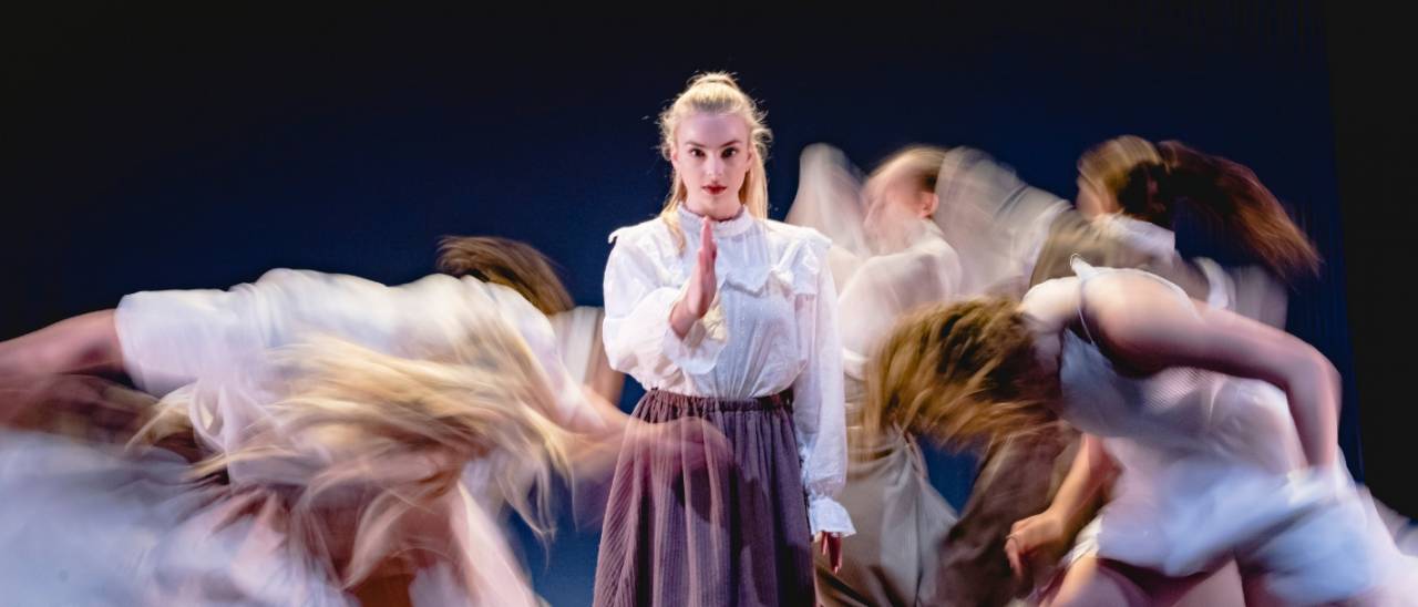 Emergence image one dancer dress in white blouse and purple long skirt walking towards the camera