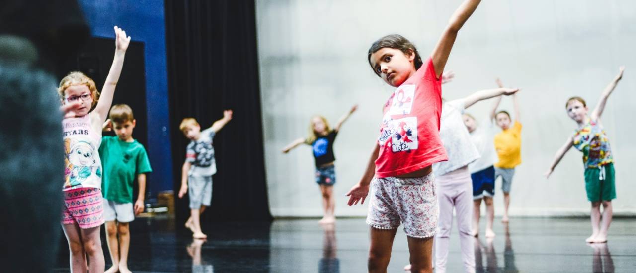 Dance image, young dancers stood with their arms in the air tilted to one side