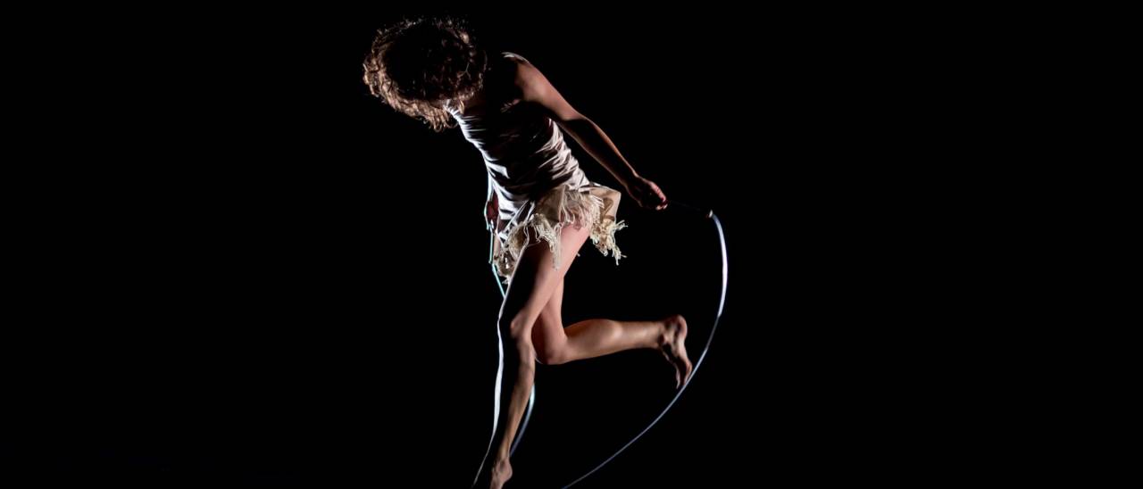 Swish image, black background dancers face on the ground, back leg in the air