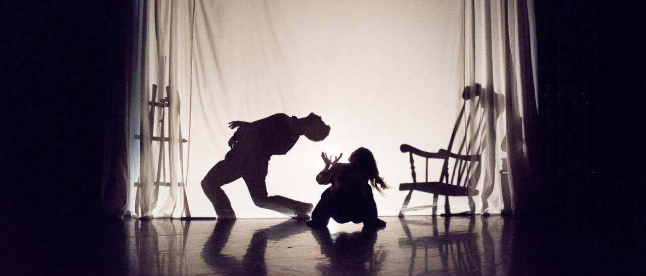 2 dancers, one as a silhouette behind a sheet and the second looking up from the floor