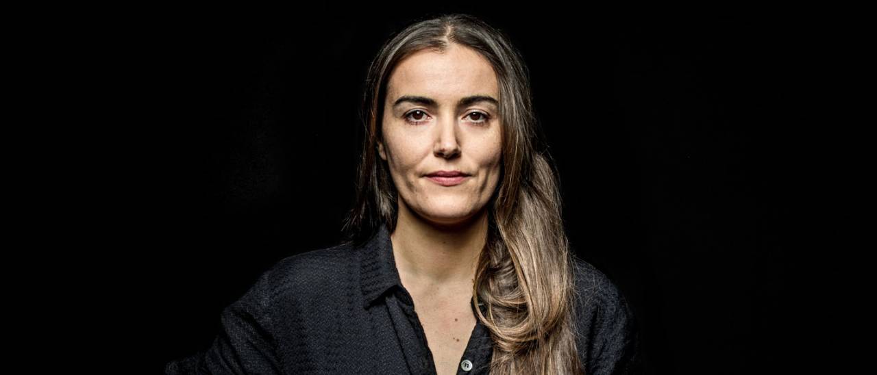 Image of Alexandra, long brown hair, tanned skin, black tshirt against a black background