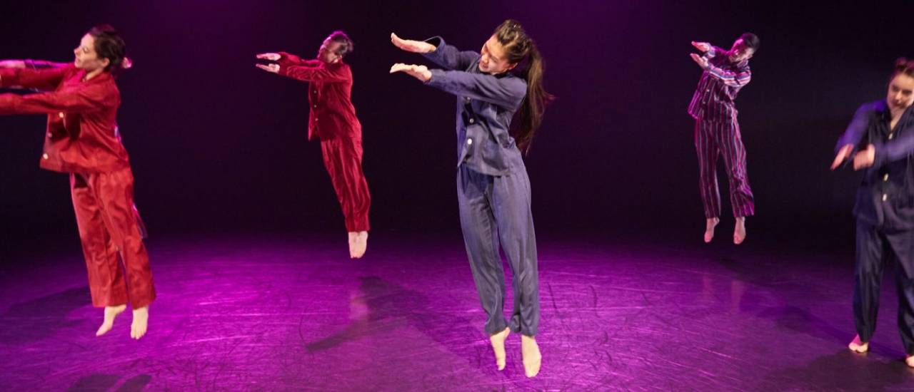 2 dancers holding hands, 1 with their leg up in the air