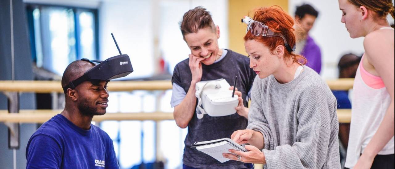 4 people looking at a notebook, 1 wearing a VR headset