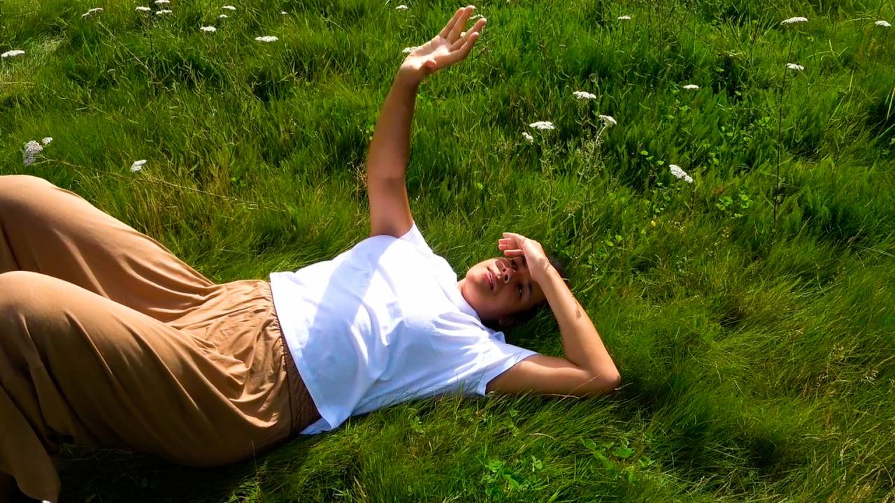 Shakeera lying in a green field with her hand towards the sun