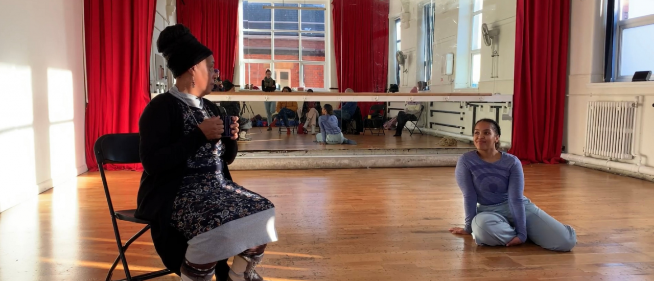 two dancers sitting in a studio with coffee smiling at one another