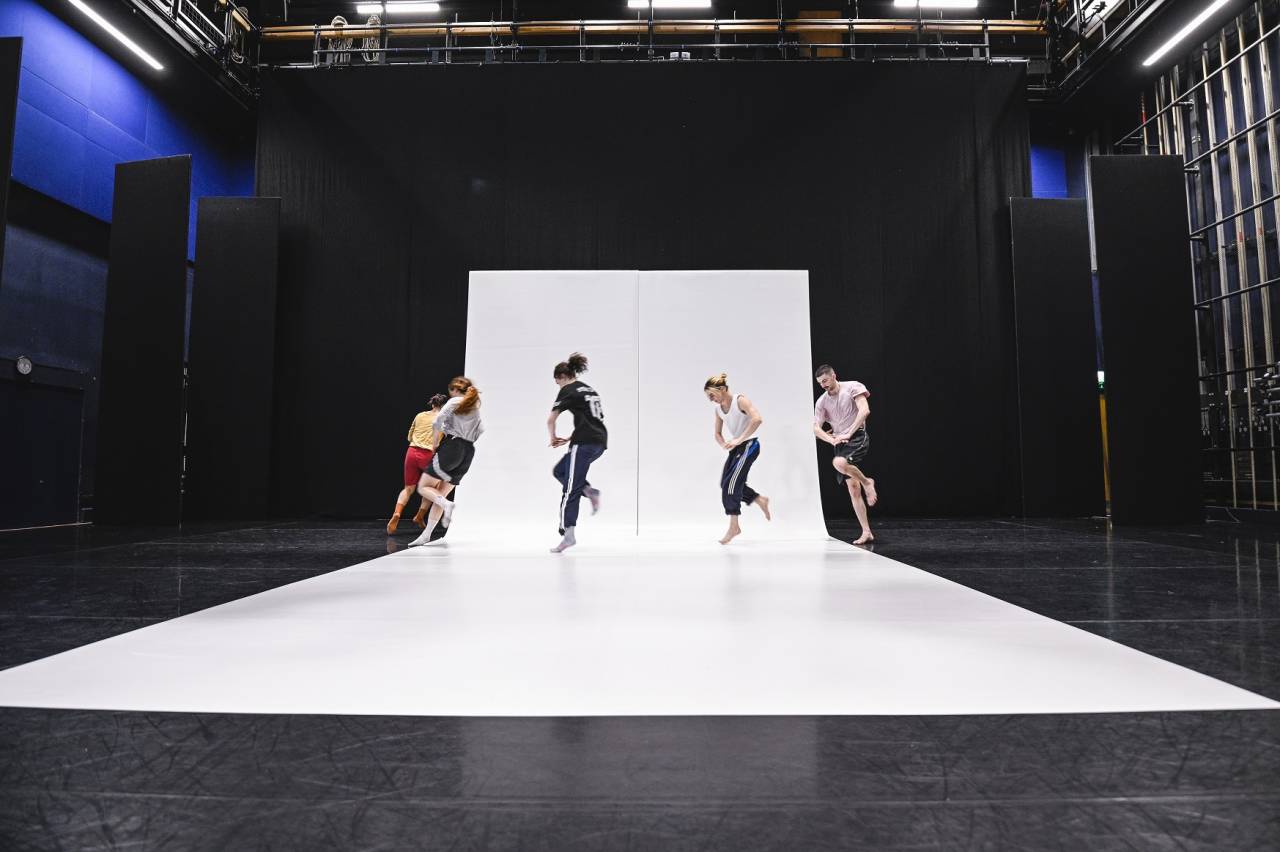 the blue room with a large prop in the middle, white dance floor is propped up and makes a wave, dancers move around it