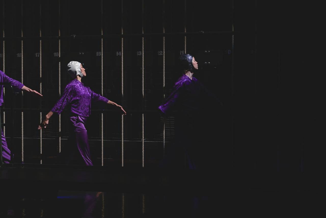 Three dancers in purple satin costumes and sparkling swim caps march perfect harmony