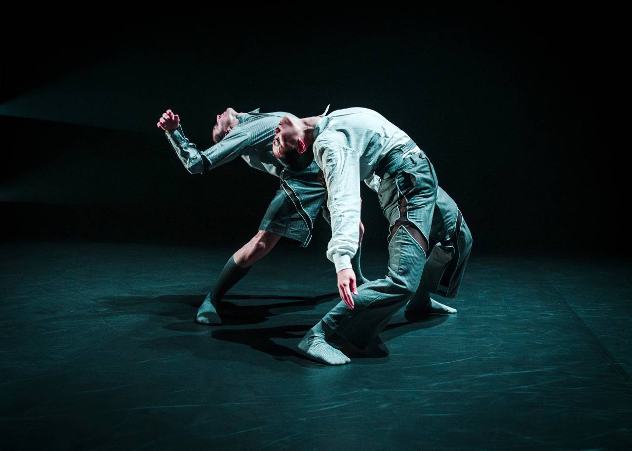 two dancers bend over backwards, one arching over the other 