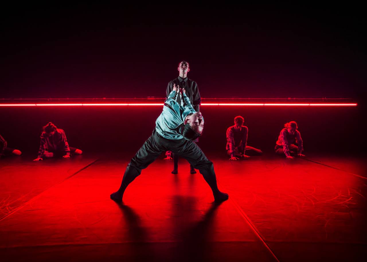 dancers bending dramatically backwards whilst others sit on the floor bathed in red light