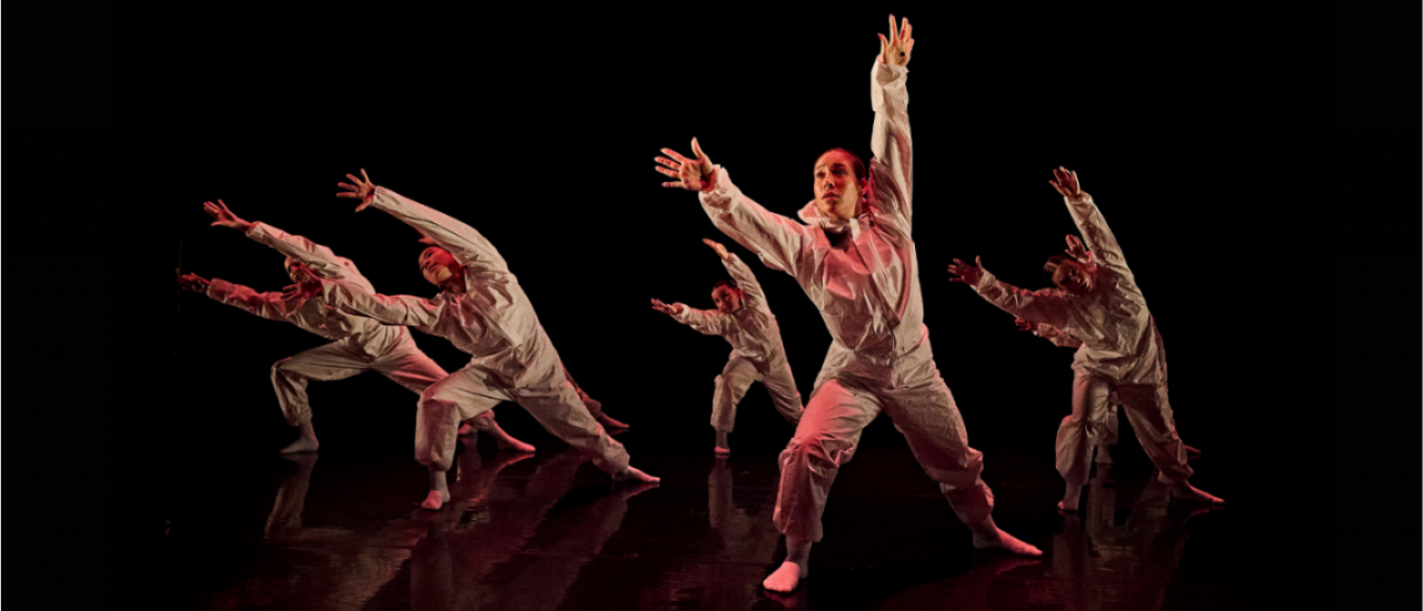 young dancers in white paper jumpsuits reaching into the air 