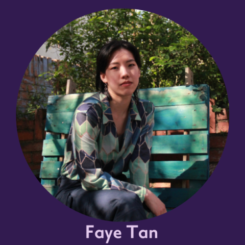 Faye wears a blue and green shirt and sits on a blue bench under glowing sunshine, she has black, short hair tucked behind her ears